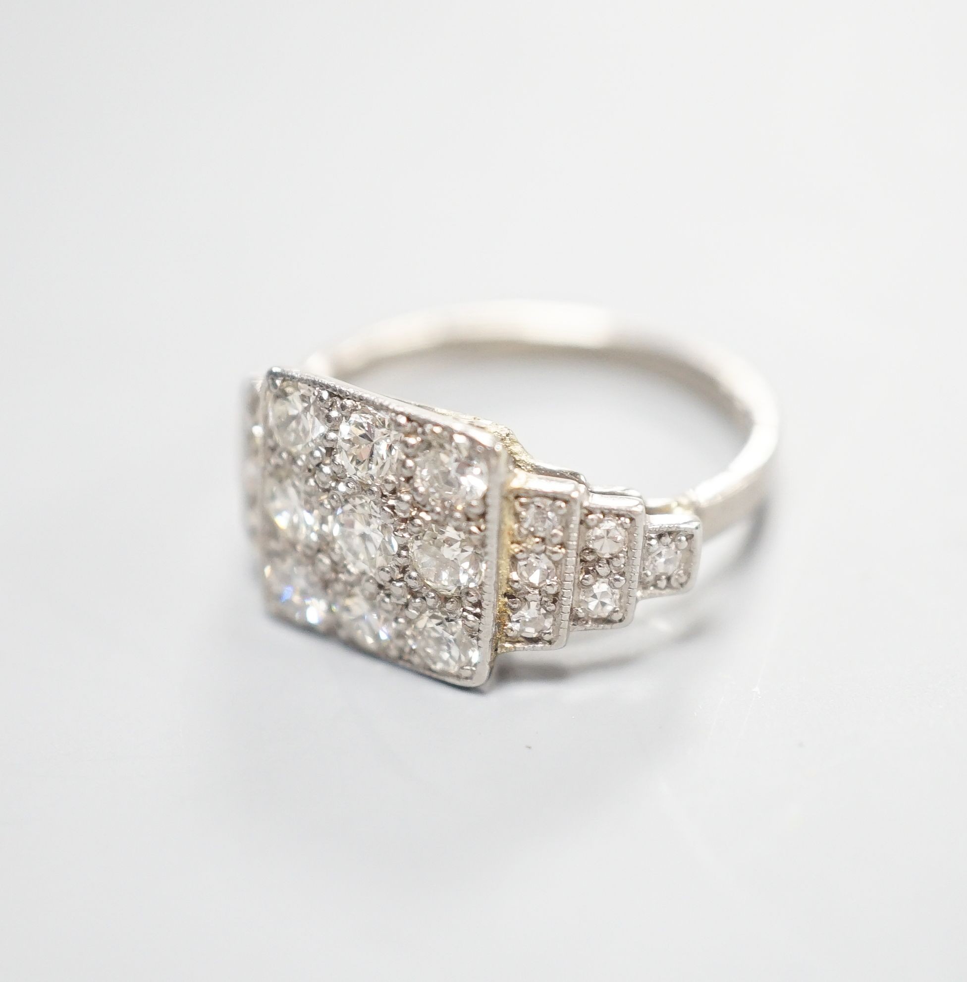 An Art Deco style white metal and nine stone diamond set tablet ring, with diamond set stepped shoulders, size K, gross weight 3.2 grams.